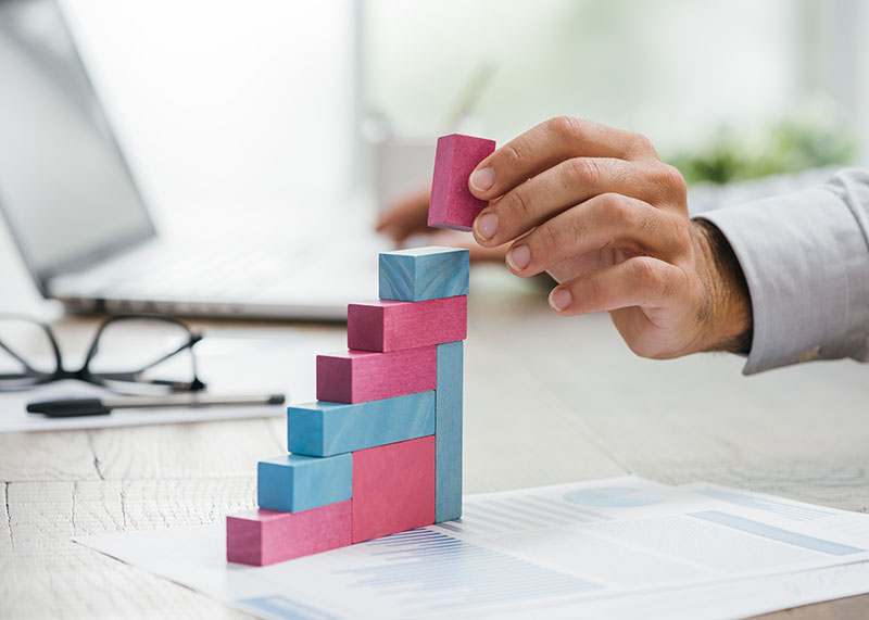 Businessman working at office desk, he is building a growing financial graph using wooden toy blocks: successful business concept