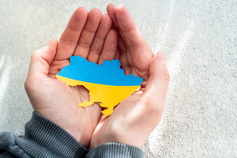 Hands holding the national flag of Ukraine in the shape of the borders of Ukraine. Support for Ukraine in the war with Russia. Stop the war concept