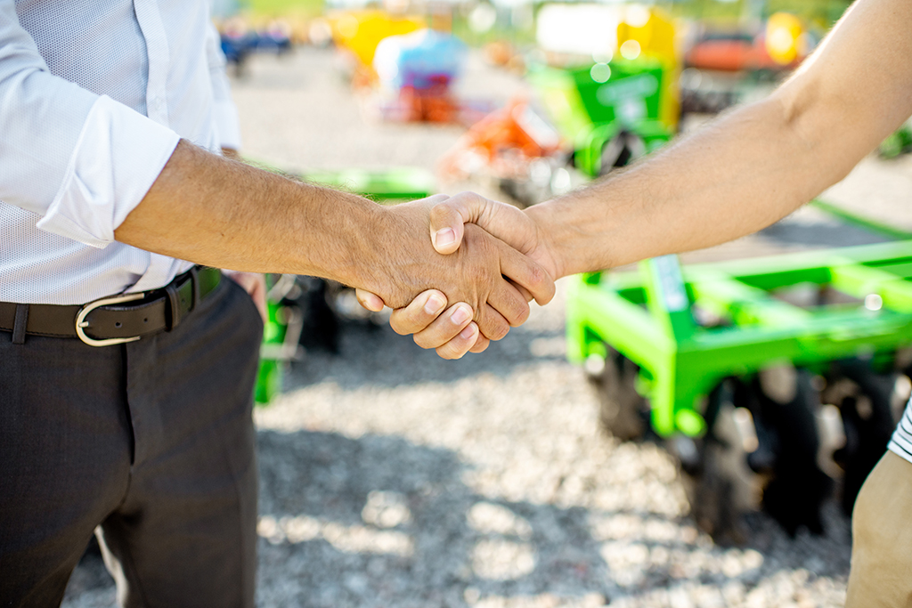 Buyer shaking hand with salesman on the open ground of the agricultural shop, having a deal, close-up view